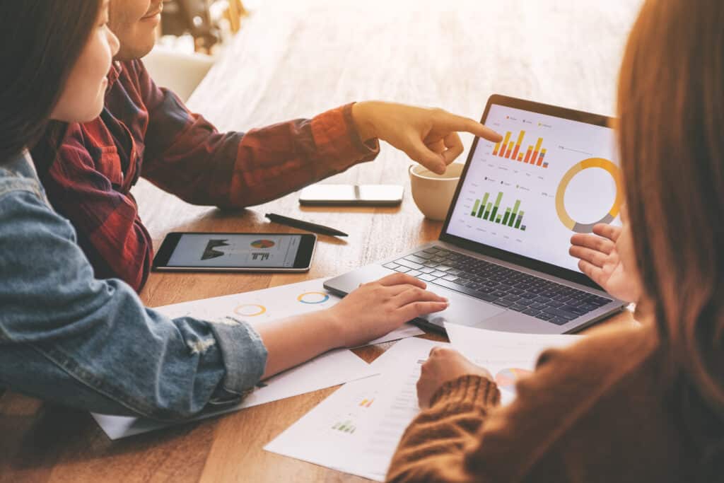 three people pointing on a laptop with a statistics chart on it