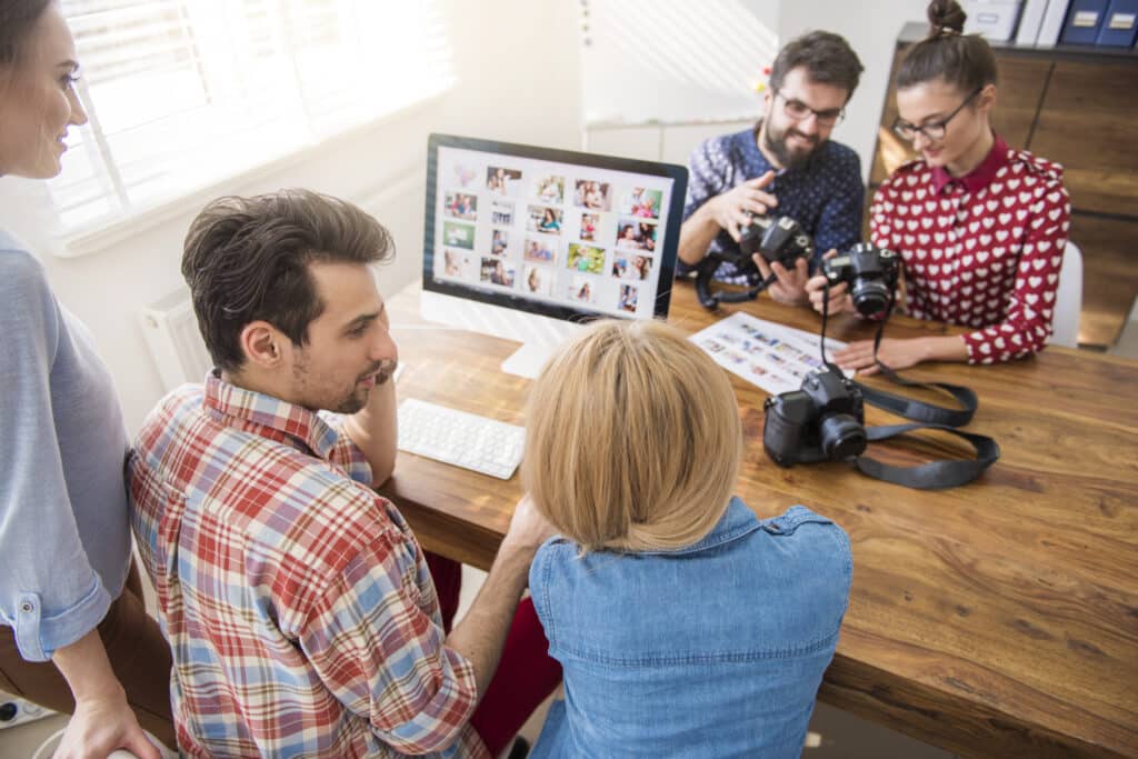 3 people in front of a monitor brainstorming and 2 people looking at their cameras