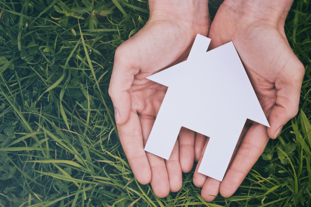 two hands holding a white house over a bed of green grass