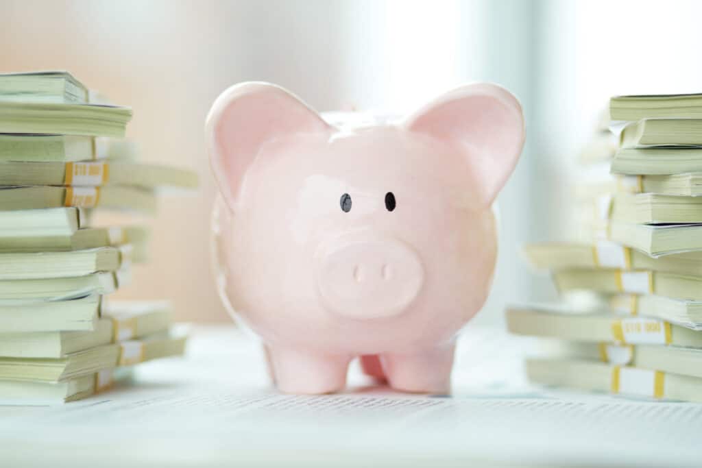 pink piggy bank surrounded by stacks of dollar bills