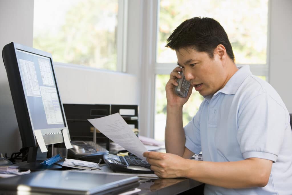 Man in home office with computer and paperwork on telephone
