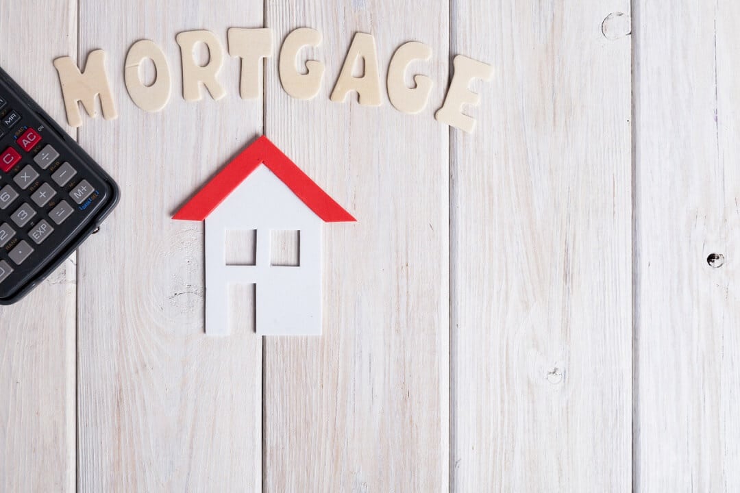 small house with calculator over white wood with the word 'Mortgage'