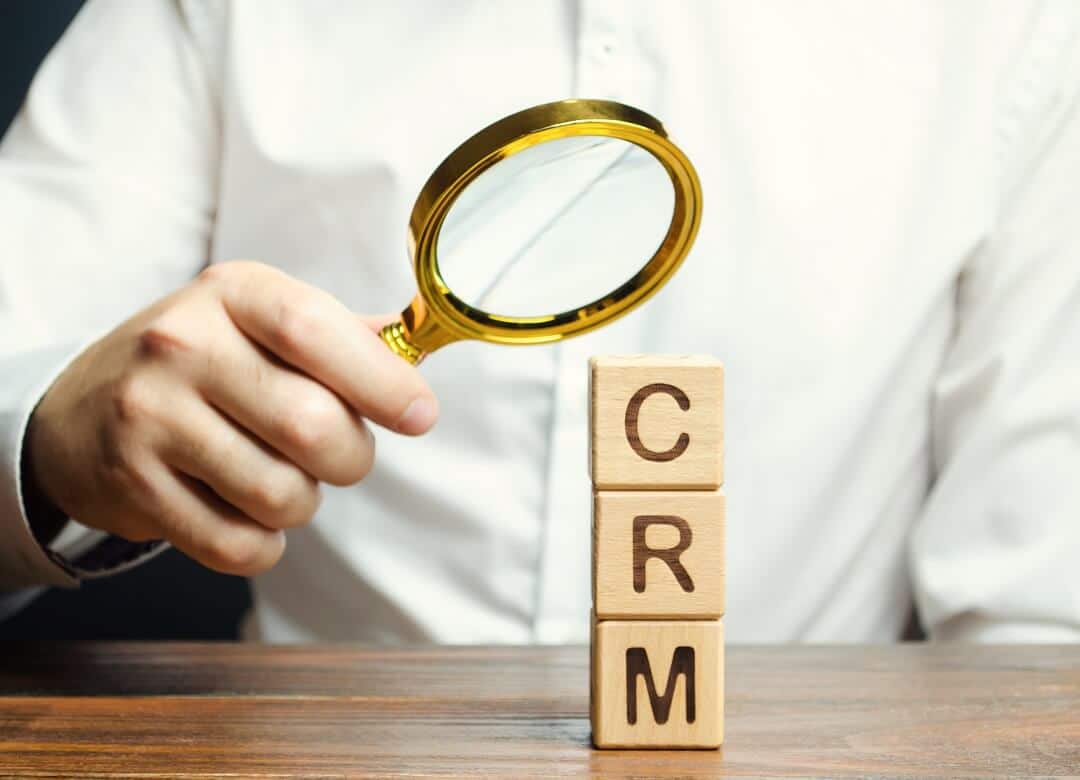 Man holding a magnifying glass on wooden blocks with the word CRM